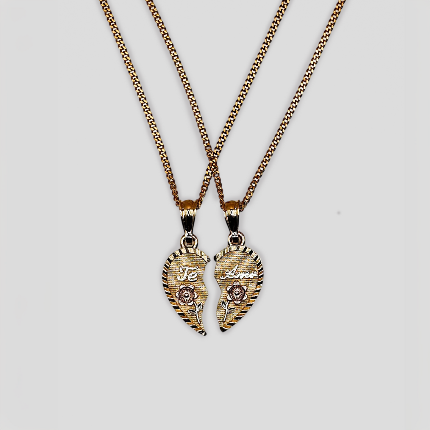 Two gold-tone necklaces featuring matching pendant halves of a broken heart. Each half is engraved with "Te Amo" and adorned with pink roses, forming a complete heart when placed together.