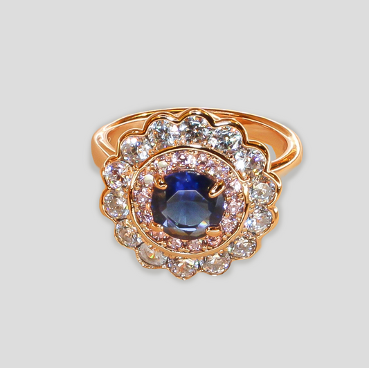 Gold-colored ring featuring a deep blue gemstone at the center, surrounded by two layers of sparkling simulant diamonds