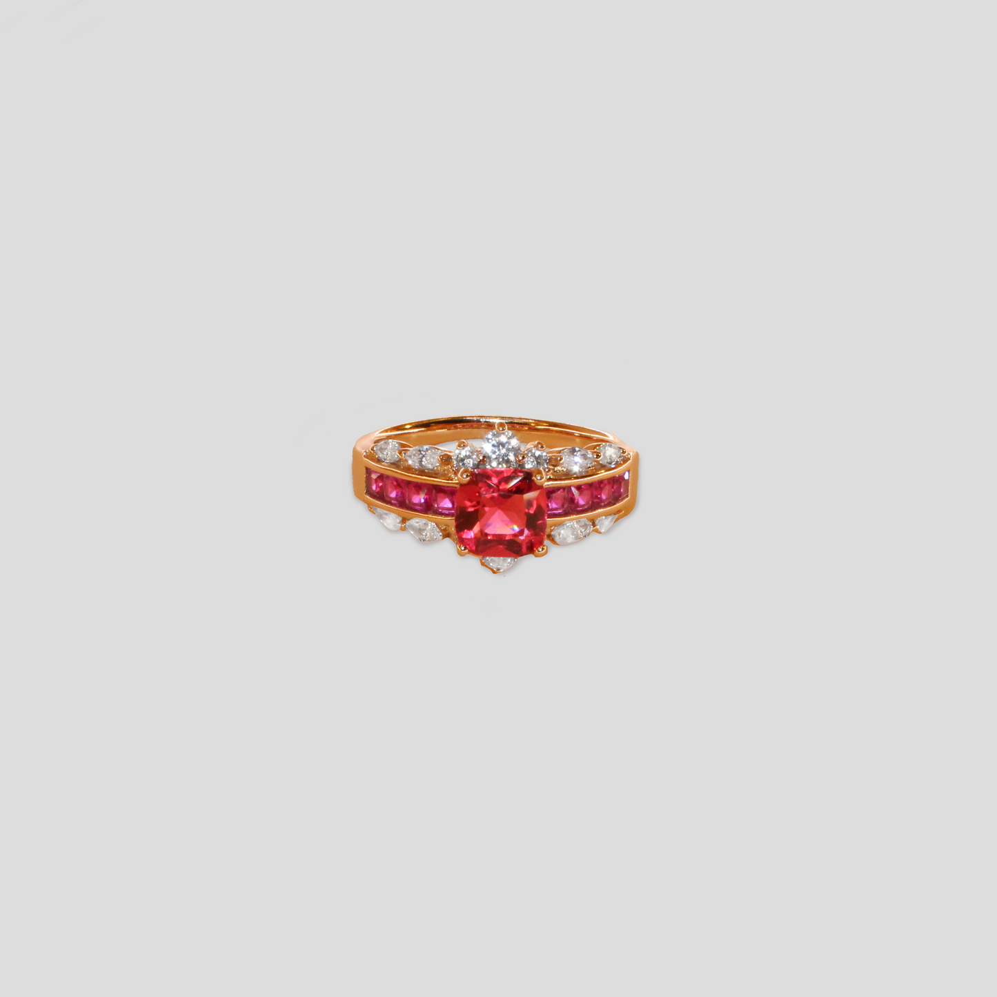 Gold-colored ring featuring a large square red gemstone, flanked by rows of smaller red stones and teardrop-shaped simulant diamonds.