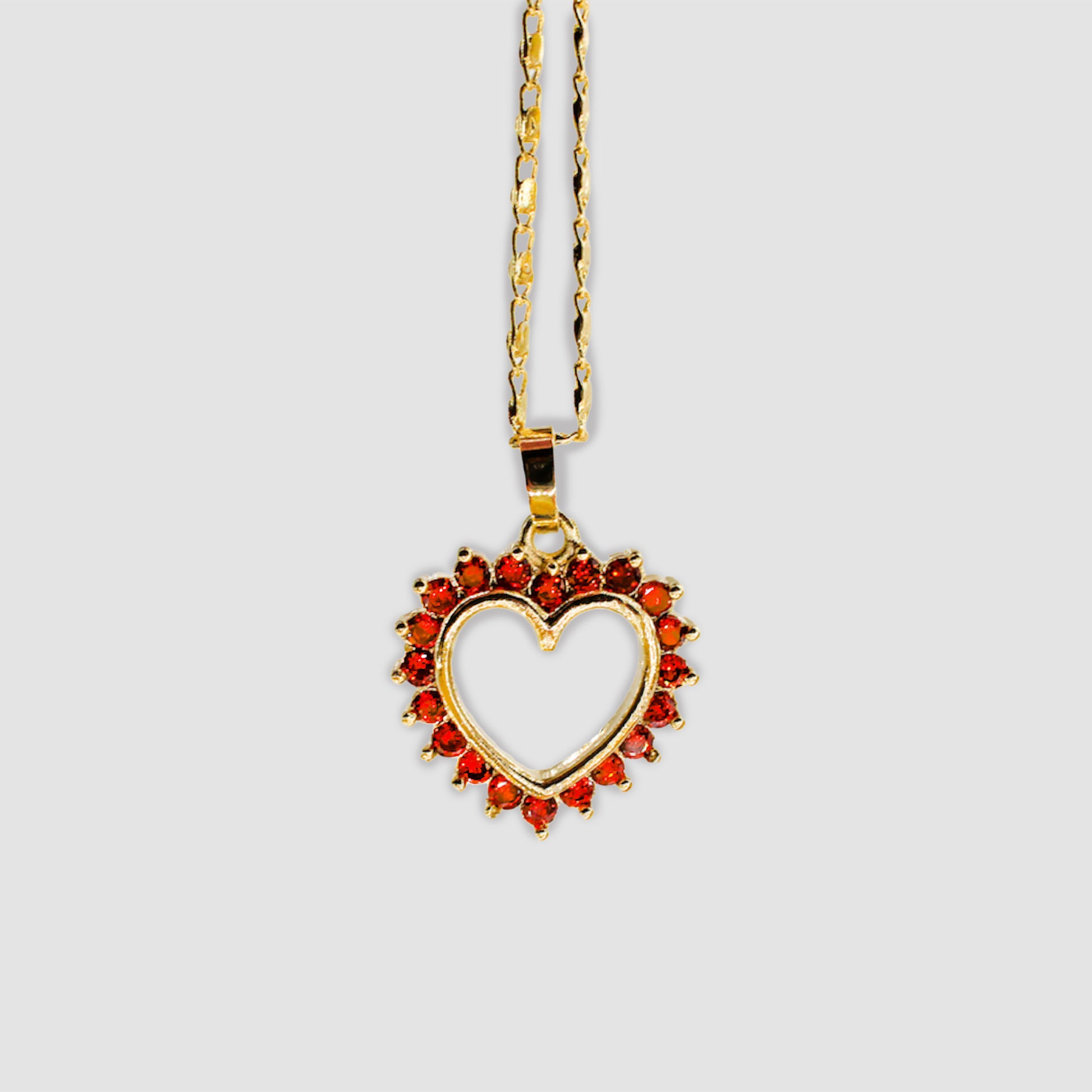 Gold-colored necklace with a heart-shaped pendant, adorned with red gemstones around the open-heart design.