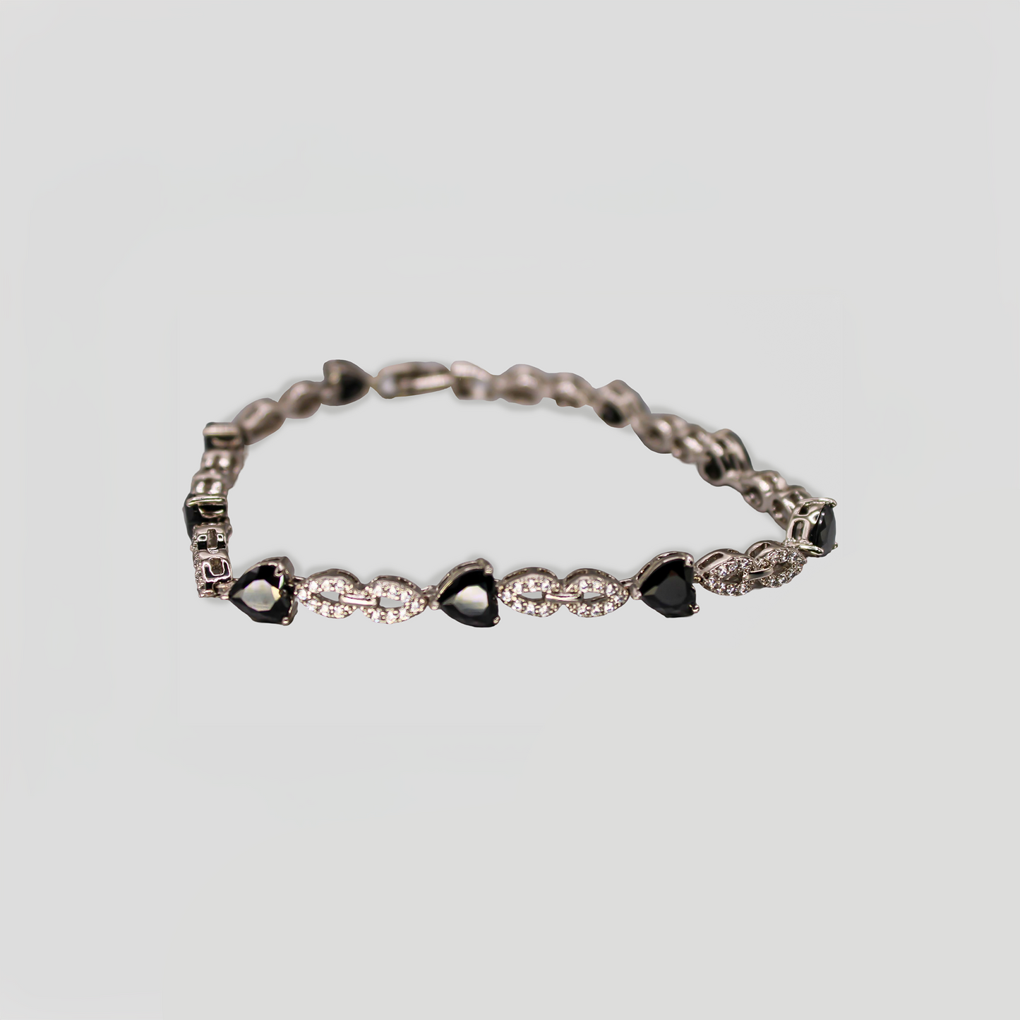 A silver-tone bracelet with heart-shaped black stones and diamond simulants, arranged in an alternating pattern with a secure clasp.