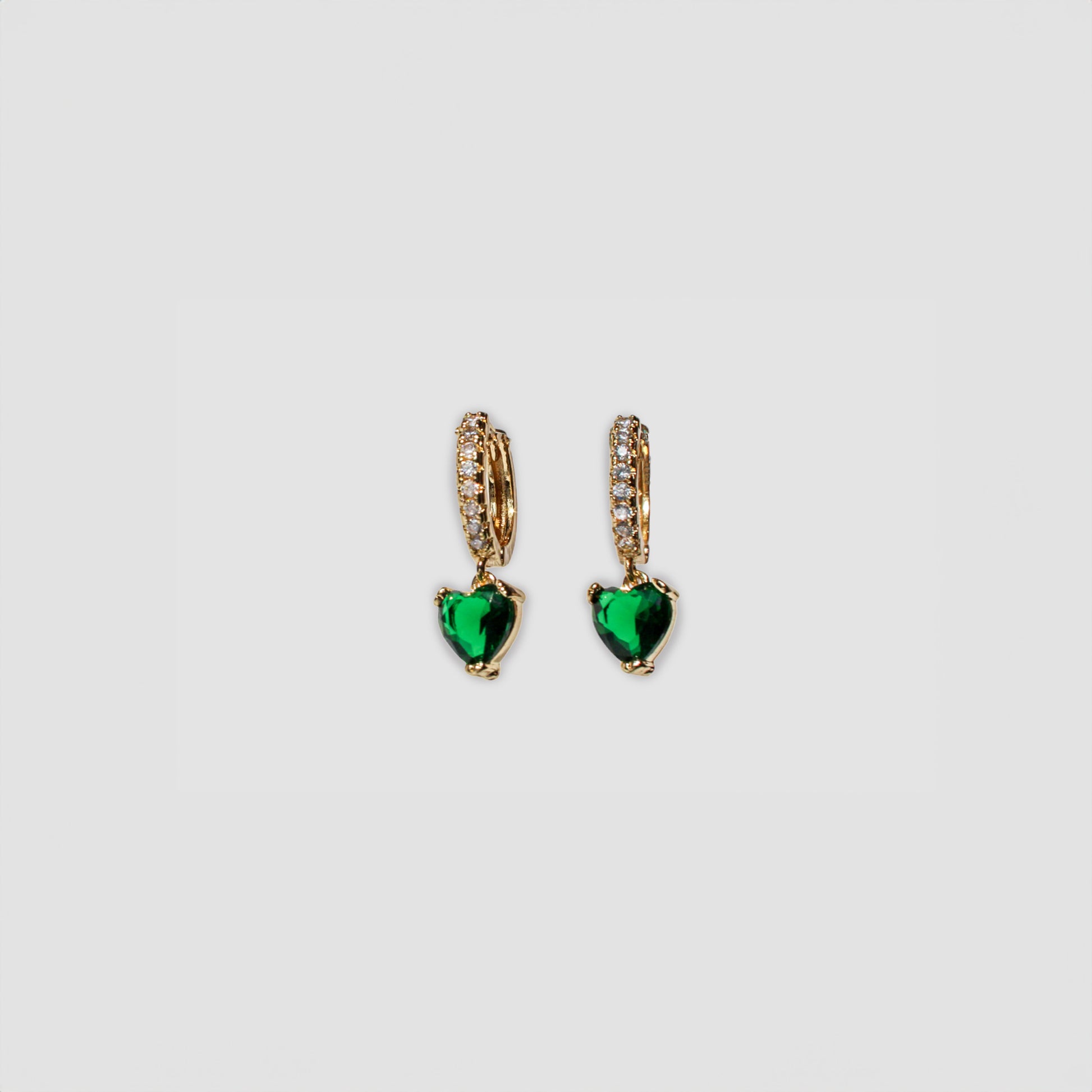 A pair of gold-colored drop earrings featuring a small row of clear gemstones along the top part and a green dangling heart-shaped gemstone at the bottom.