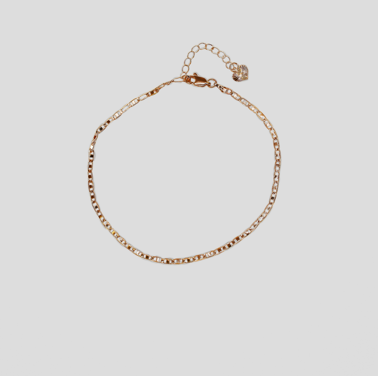 A delicate gold-colored bracelet featuring a simple, thin chain with small, flat links. It has an adjustable clasp with an extension chain ending in a small heart-shaped charm.