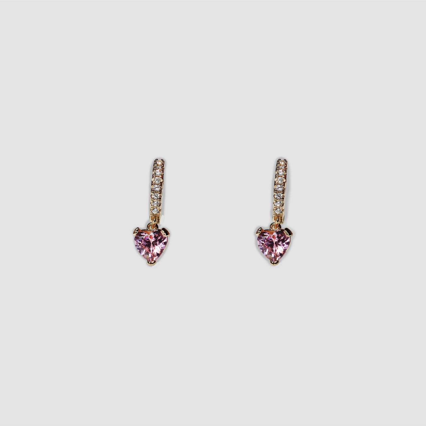 A pair of gold-colored drop earrings featuring a small row of clear gemstones along the top part and a pink dangling heart-shaped gemstone at the bottom.