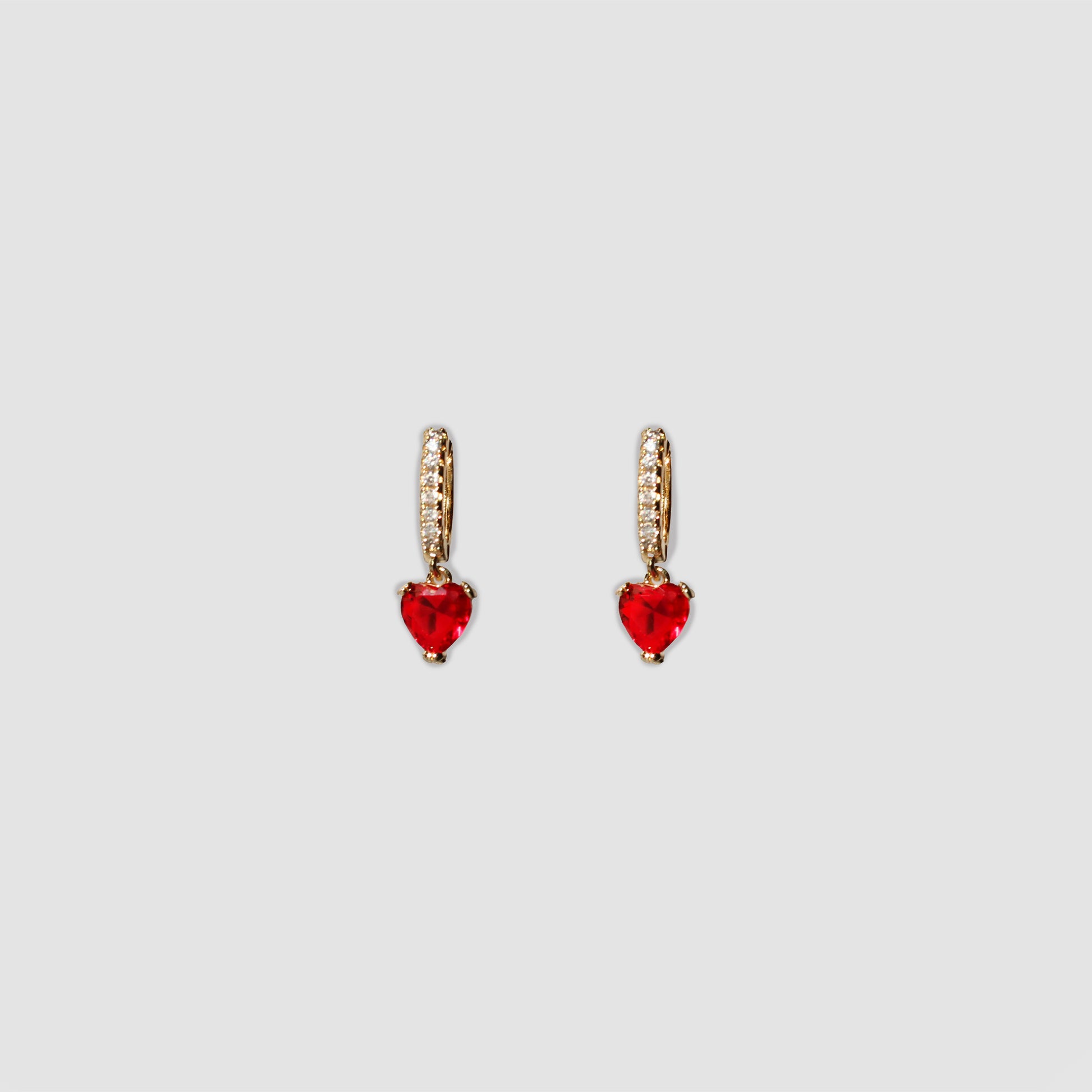 A pair of gold-colored drop earrings featuring a small row of clear gemstones along the top part and a ruby dangling heart-shaped gemstone at the bottom.