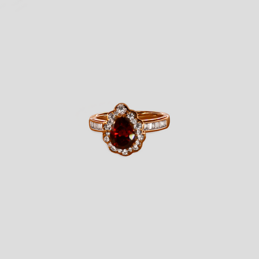 Gold-colored ring with a teardrop-shaped red gemstone, surrounded by simulant diamonds.