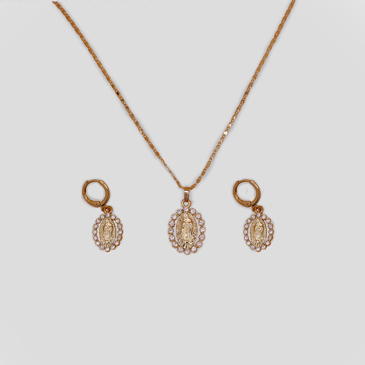 A gold color necklace and earrings set featuring the Virgin Mary. All three has the same design of a oval Virgin Mary with white simulate gemstones