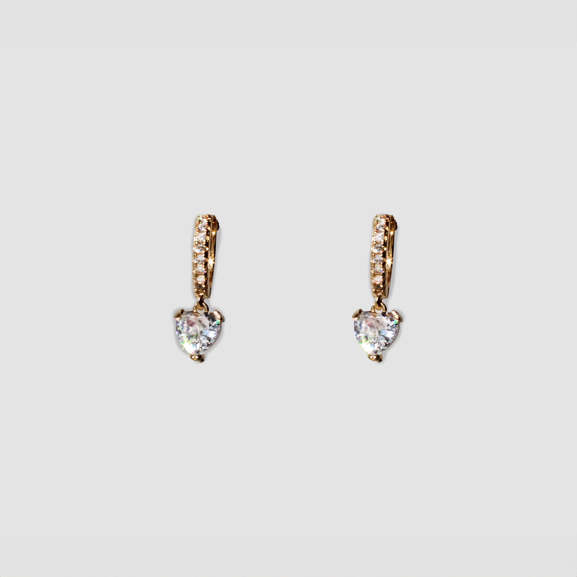 A pair of gold-colored drop earrings featuring a small row of clear gemstones along the top part and a white dangling heart-shaped gemstone at the bottom.